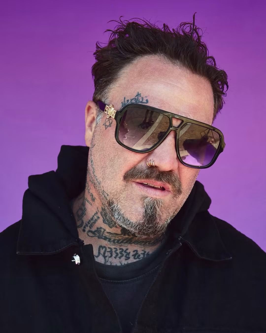 Bam Margera portrait in sunglasses against a purple background.