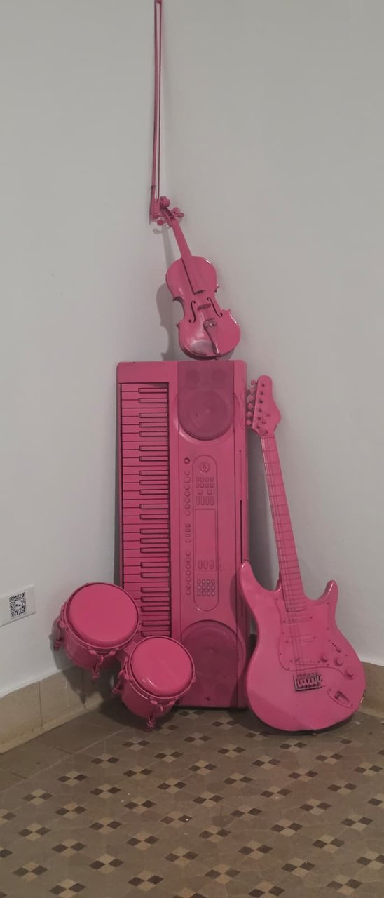 Pink-painted guitar, keyboard, violin and bongos in a corner.